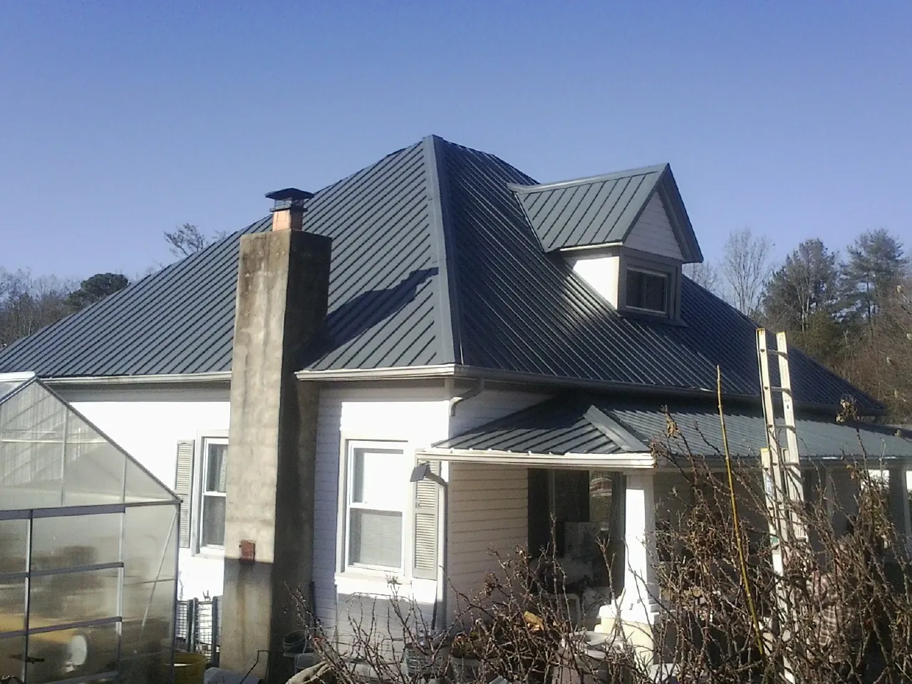 Dark blue standing seam metal roof on a white farmhouse with dormer — Slate & Tile Roof Repair by Roofing Brothers in Bon Air
