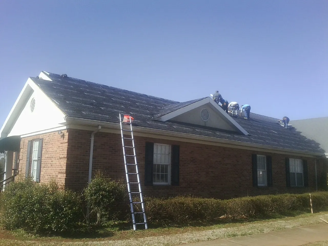 Crew tearing shingles off a brick ranch roof with a ladder set — Emergency Roof Repair work by our crew in Bon Air