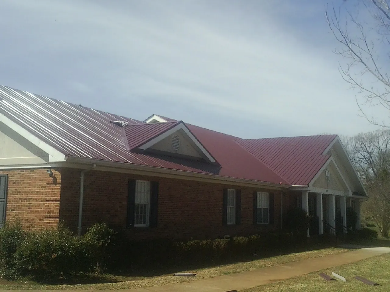 Red metal roof with gabled entries on a long brick building, from a Hail Damage Roof Repair job in Bon Air
