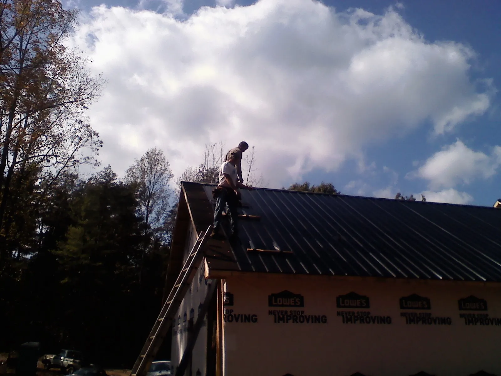 Roofer fastening dark metal panels high against a cloudy sky, from a Roof Inspection job in Bon Air