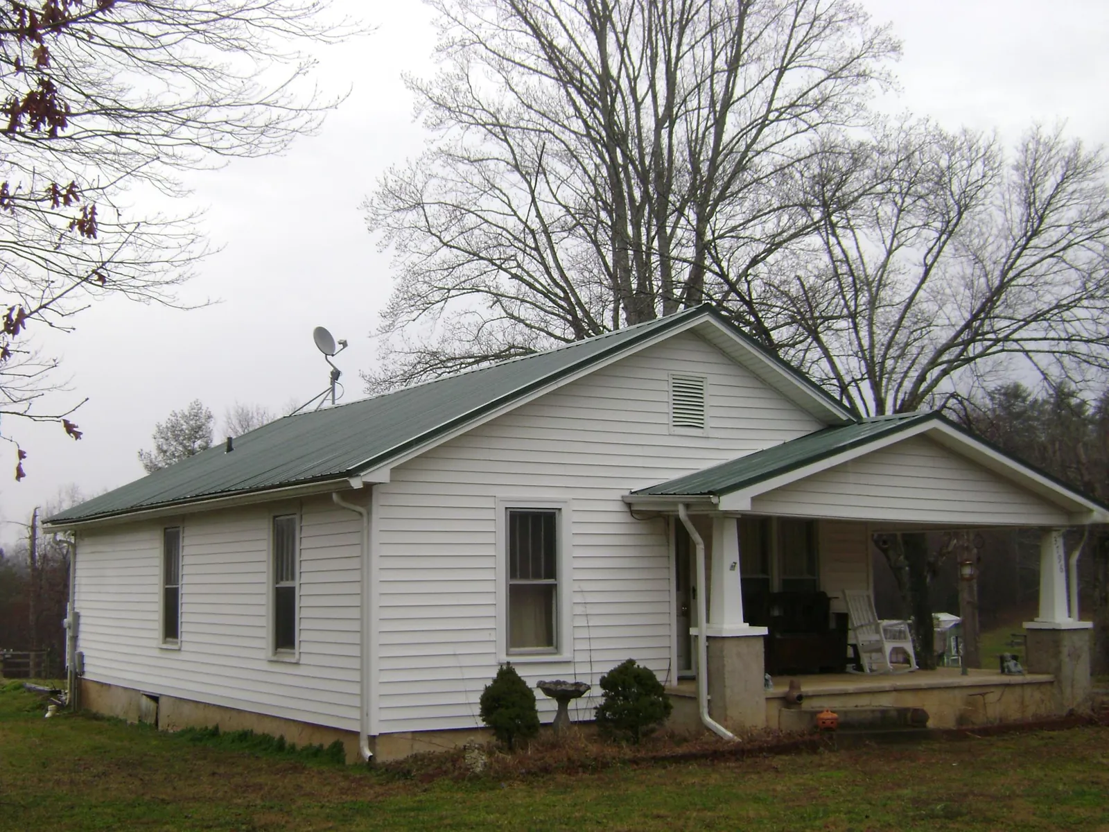 Green metal roof on a white bungalow with a side porch in Bon Air