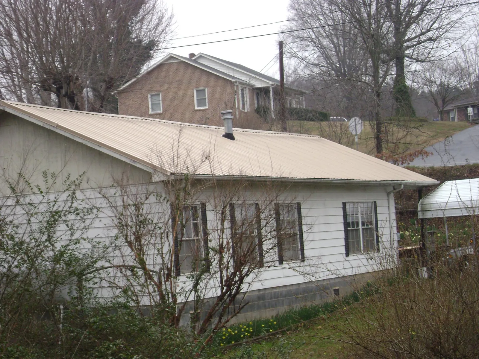 Tan metal roof on a white sided house set into a hillside — Commercial Roofing by Roofing Brothers in Bon Air